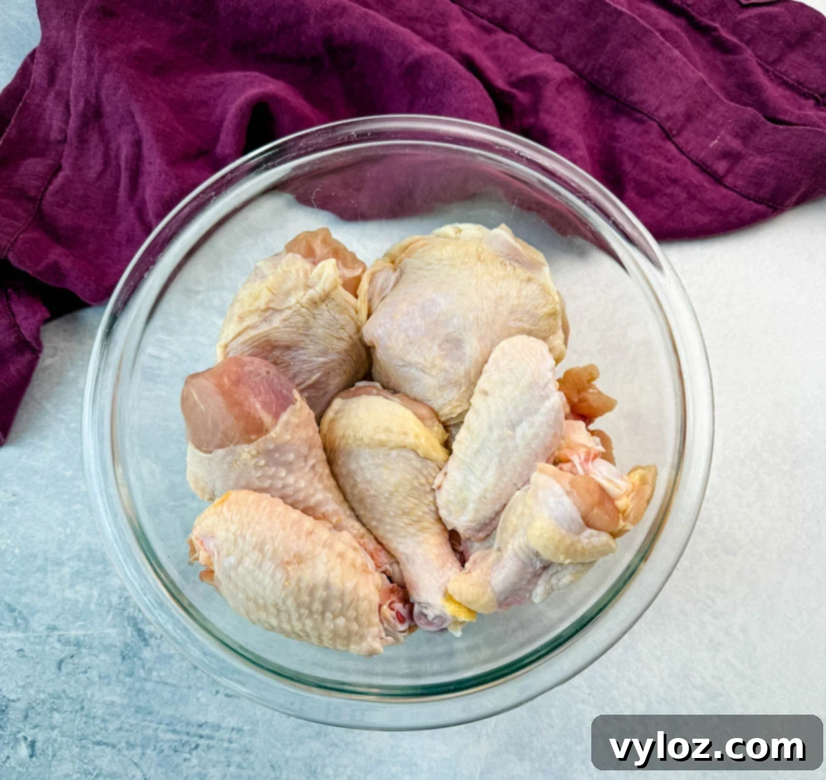 Raw chicken pieces, including drumsticks, wings, and thighs, placed in a large clear glass bowl, ready to be seasoned and breaded.