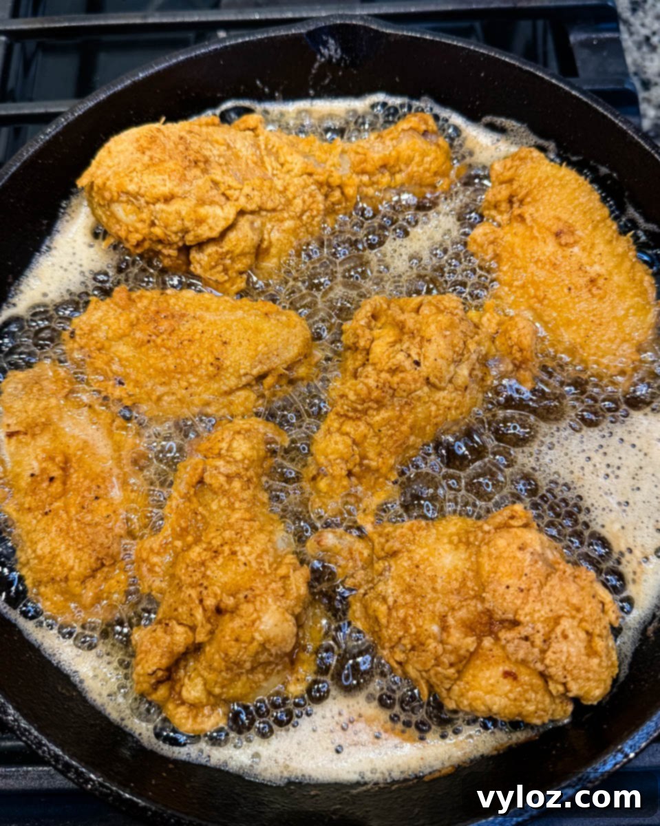 Overhead shot of golden fried chicken pieces frying in hot oil in a cast iron skillet on the stovetop.
