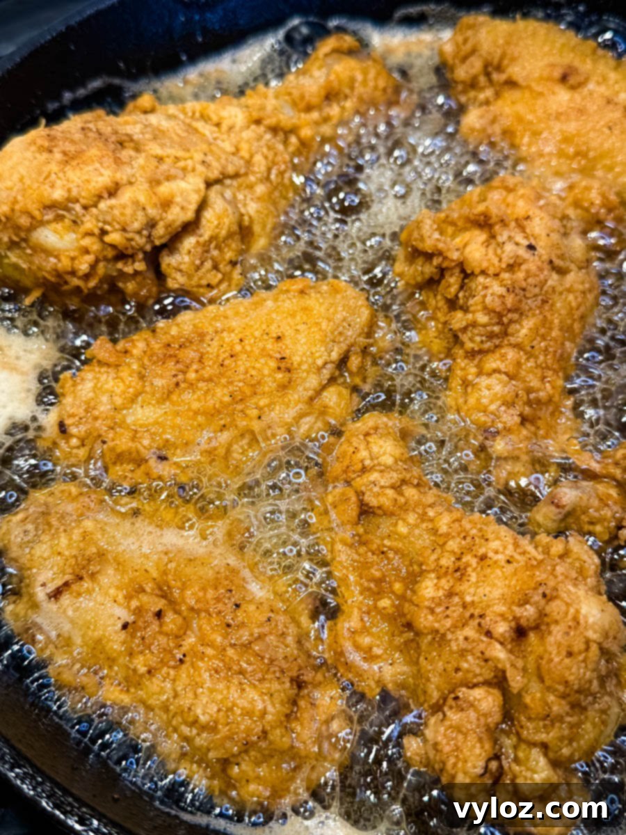 Fried chicken sizzling in a cast iron skillet filled with bubbling hot oil. The breading is crisping up to a deep golden color.