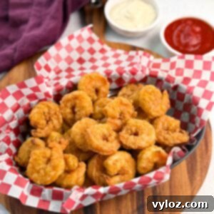 Red and white checkered basket brimming with breaded fried shrimp, photographed at an angle to highlight texture and quantity.