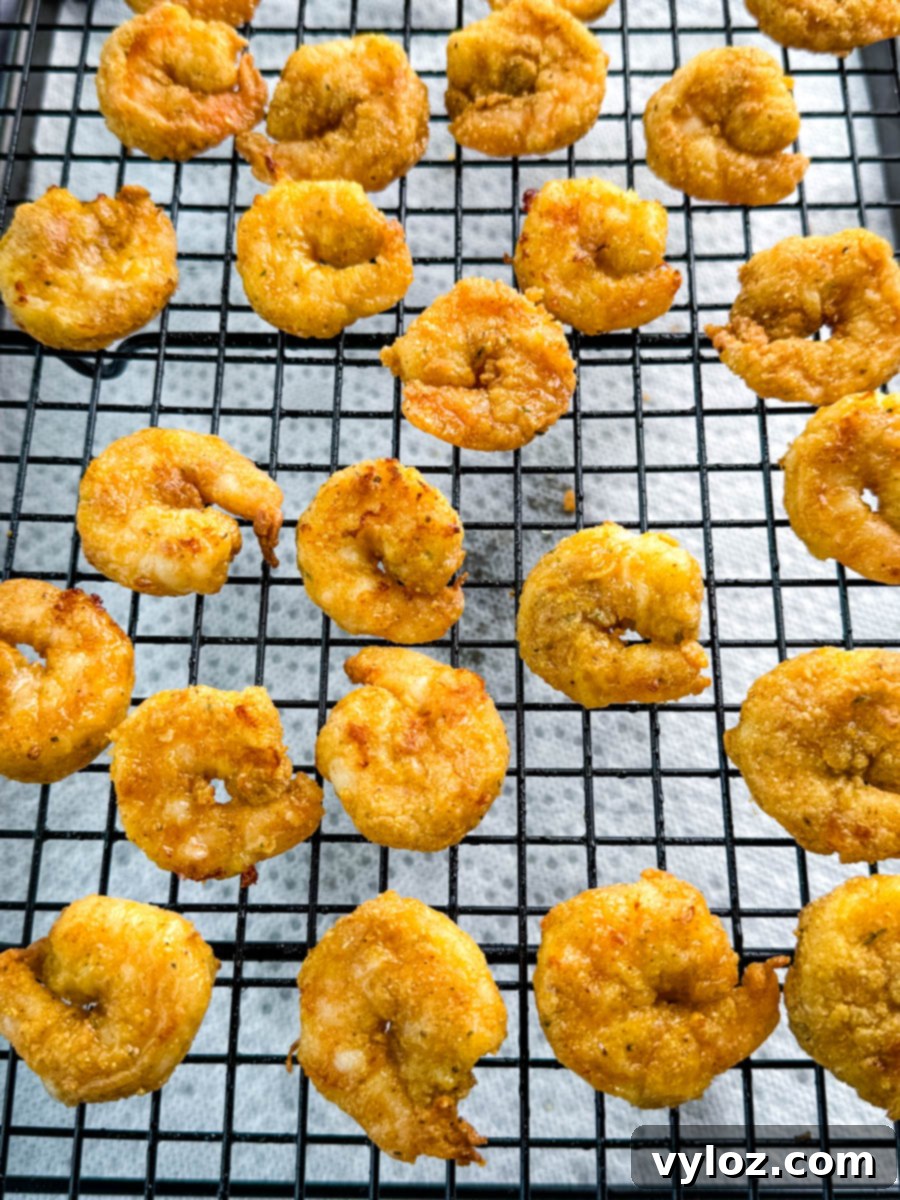 Crispy breaded shrimp cooling on a wire rack after frying, spaced evenly to preserve crispness.