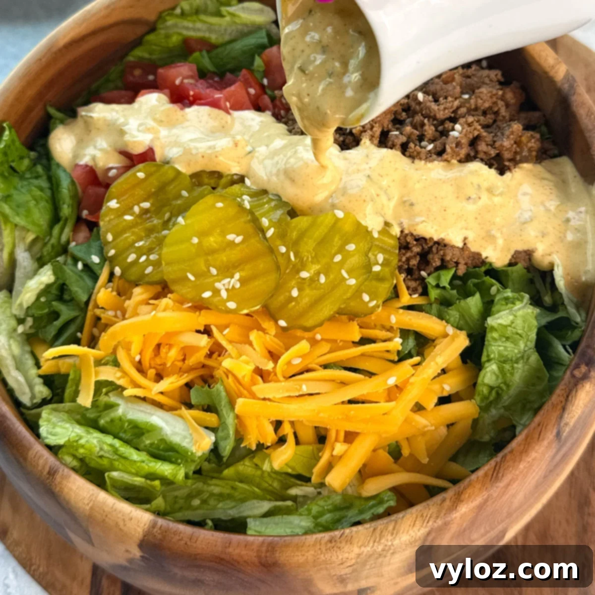 Homemade Big Mac sauce generously drizzled over a fresh burger salad bowl, showcasing its creamy texture.