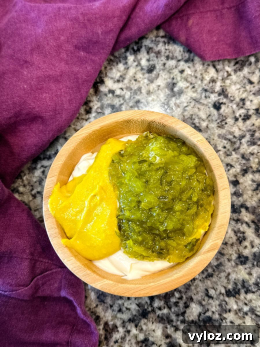 A wooden bowl displaying unmixed layers of creamy mayonnaise, bright yellow mustard, and chunky sweet pickle relish, arranged side by side on a polished granite countertop.