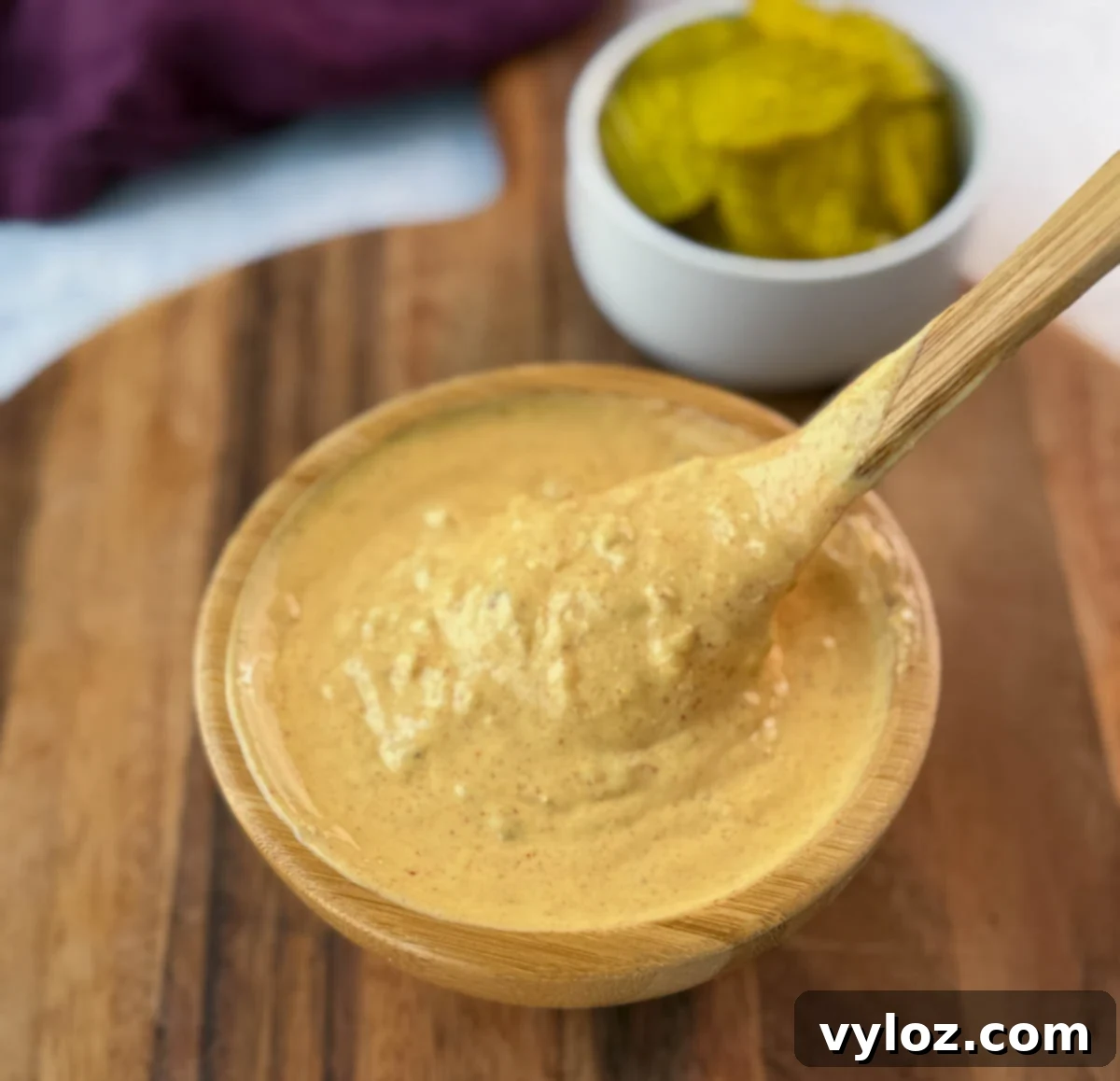 Close-up of a spoon lifting and expertly drizzling creamy Big Mac sauce from a wooden bowl onto a wooden cutting board, highlighting its perfect texture.