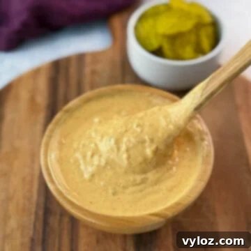 Close-up of a spoon lifting and drizzling Big Mac sauce from a wooden bowl on a wooden cutting board.
