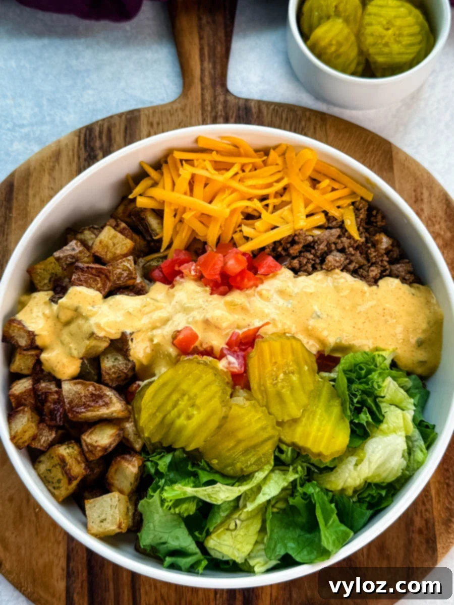 A fully assembled Big Mac bowl with crispy potatoes, seasoned ground beef, cheddar, pickles, lettuce, tomatoes, and a generous drizzle of homemade Big Mac sauce.