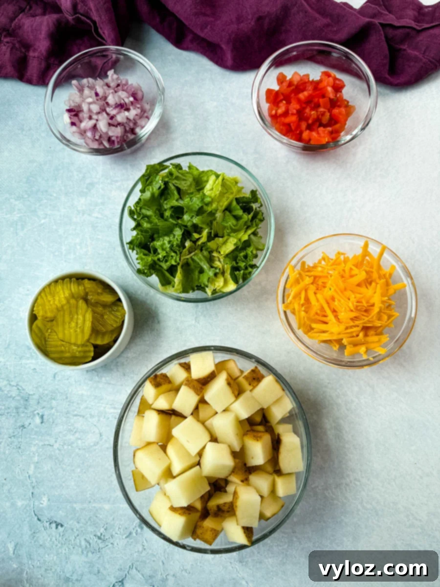 Flat lay of prepped ingredients for Big Mac bowls: diced red onion, chopped tomatoes, shredded lettuce, sliced pickles, shredded cheddar cheese, and diced raw potatoes in small glass bowls.