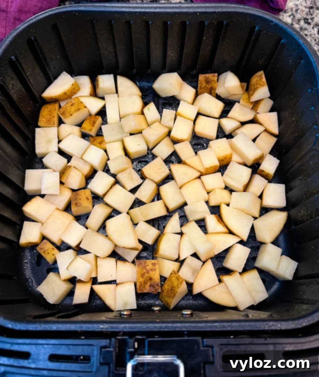 Raw diced potatoes spread evenly in an air fryer basket, seasoned and ready to cook.