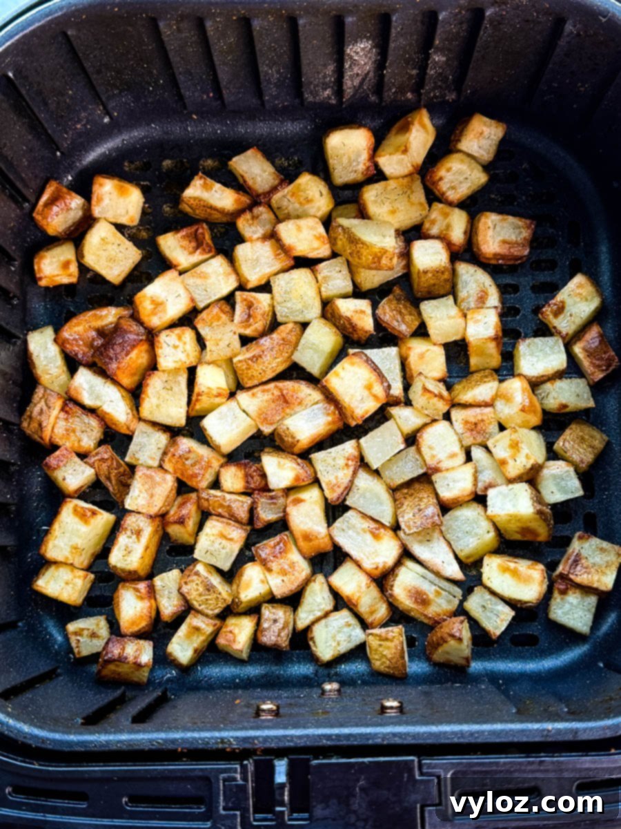 Golden brown diced potatoes cooked in an air fryer basket, evenly crisped and ready to serve.