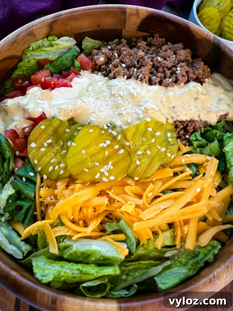 Close-up of a Big Mac salad served in a wooden bowl, topped with ground beef, diced tomatoes, shredded cheddar, pickles, sesame seeds, and drizzled with creamy Big Mac sauce.
