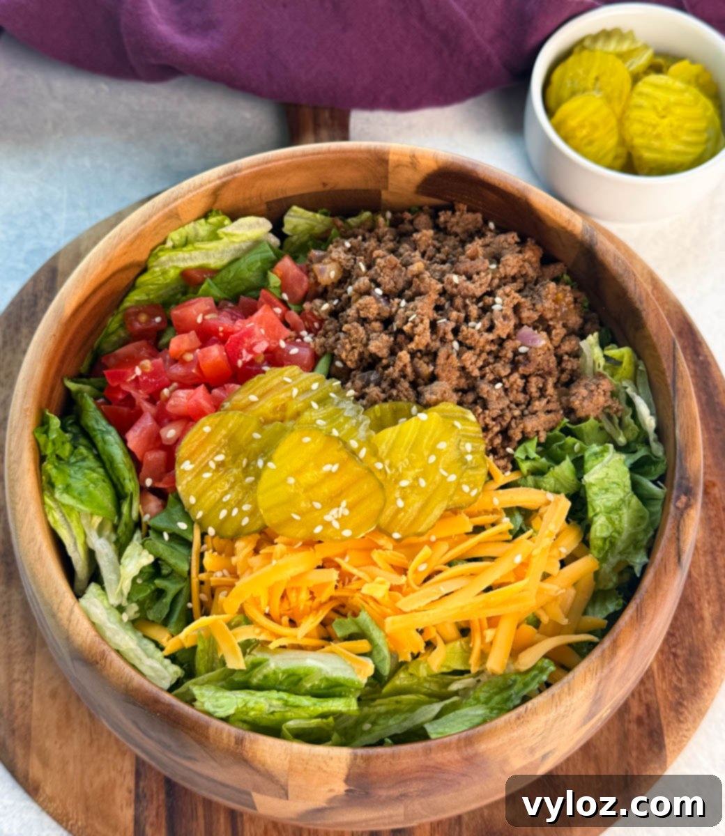 Overhead view of a Big Mac salad loaded with seasoned beef, tomatoes, shredded lettuce, cheddar cheese, and pickles, served in a wooden bowl with sesame seeds on top.