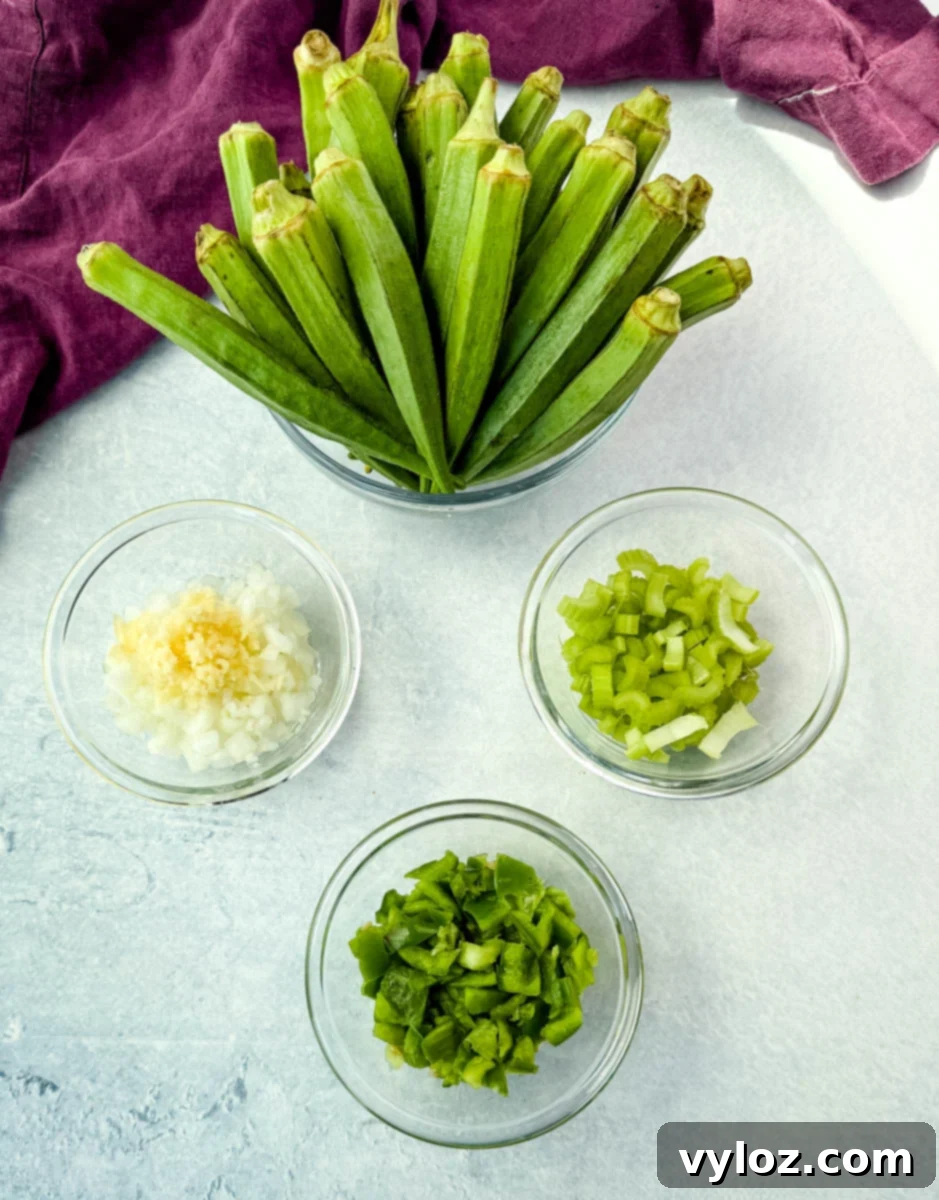Fresh whole okra next to bowls of diced onion with garlic, chopped celery, and green bell pepper.
