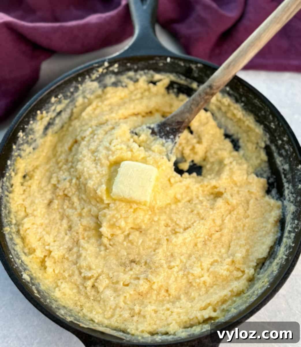 Stone ground cheese grits being stirred in a black cast iron skillet with a chunk of butter melting in the center.