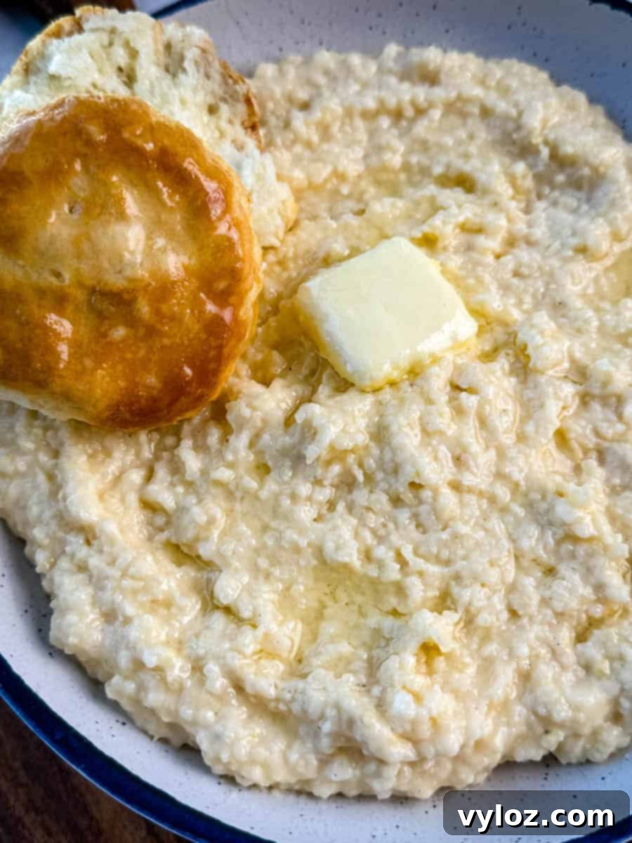 Southern-style cheese grits served in a white bowl with blue trim, finished with melted butter and a biscuit for dipping.