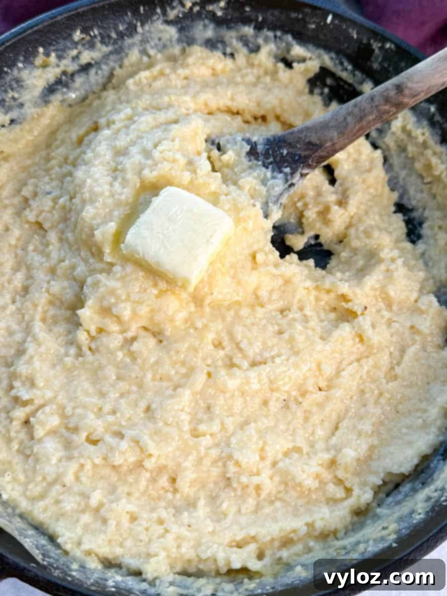 Thick and creamy cheese grits in a cast iron skillet, stirred with a wooden spoon and topped with a pat of butter.