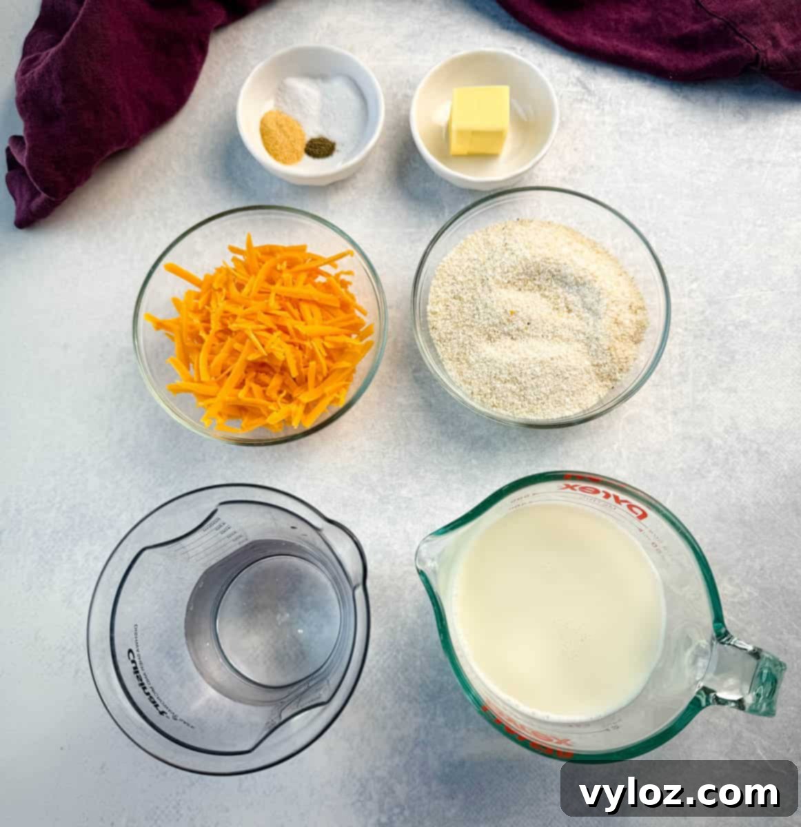 Overhead view of measured ingredients for Southern cheese grits, including shredded cheddar, dry grits, milk, butter, garlic powder, salt, and pepper.