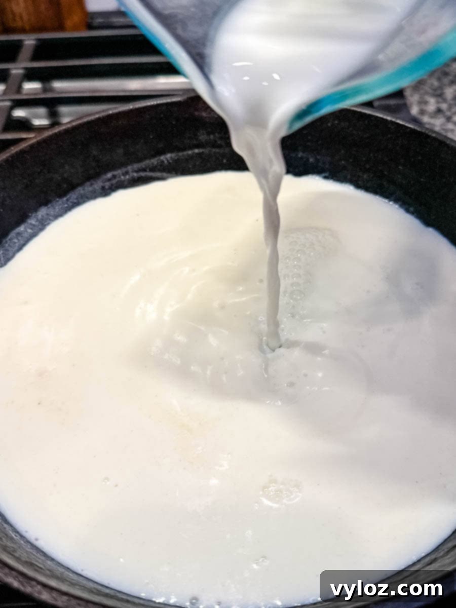 Milk being poured from a glass measuring cup into a cast iron skillet to start cooking creamy stone ground grits.