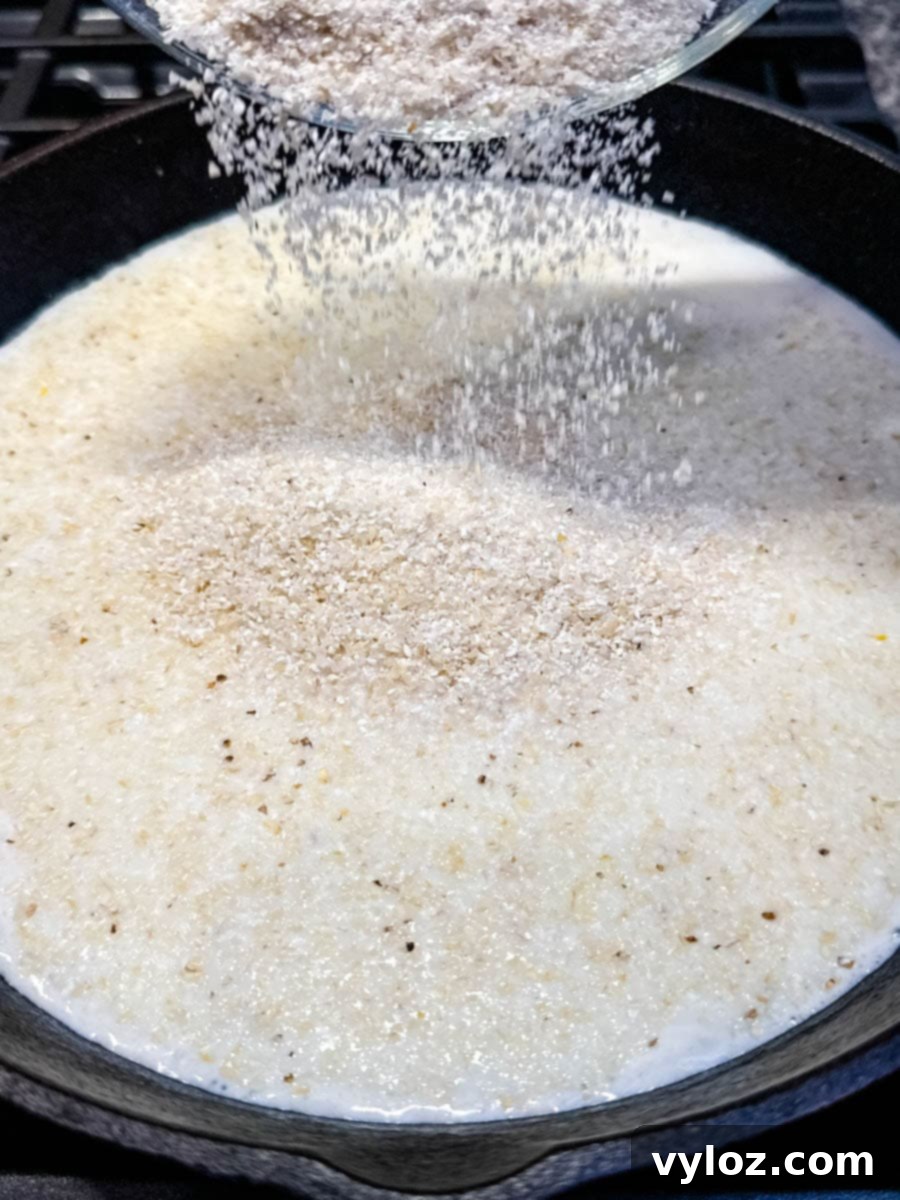 Dry stone ground grits being poured from a bowl into a cast iron skillet filled with simmering milk and water.