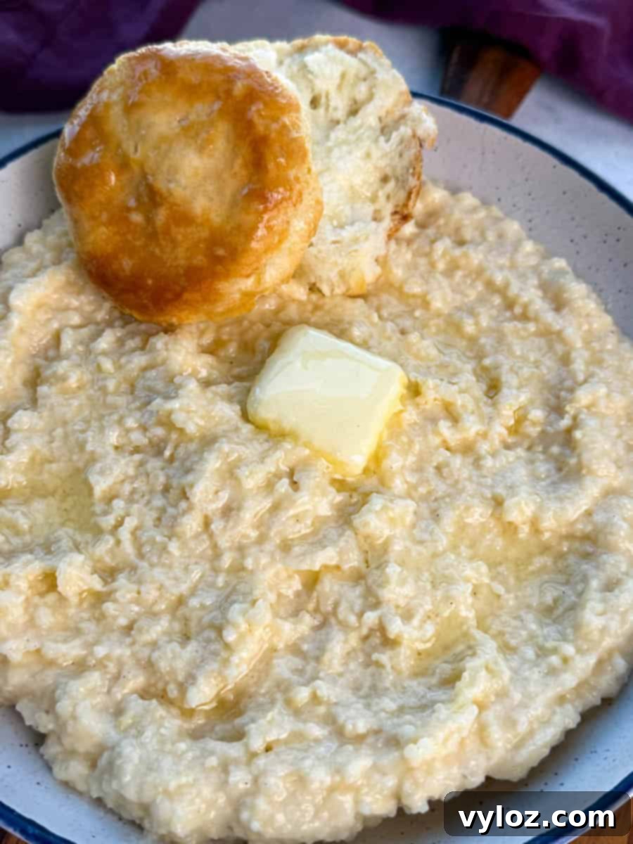 Creamy cheese grits in a bowl with a pat of butter melting on top and a fluffy biscuit resting along the rim.