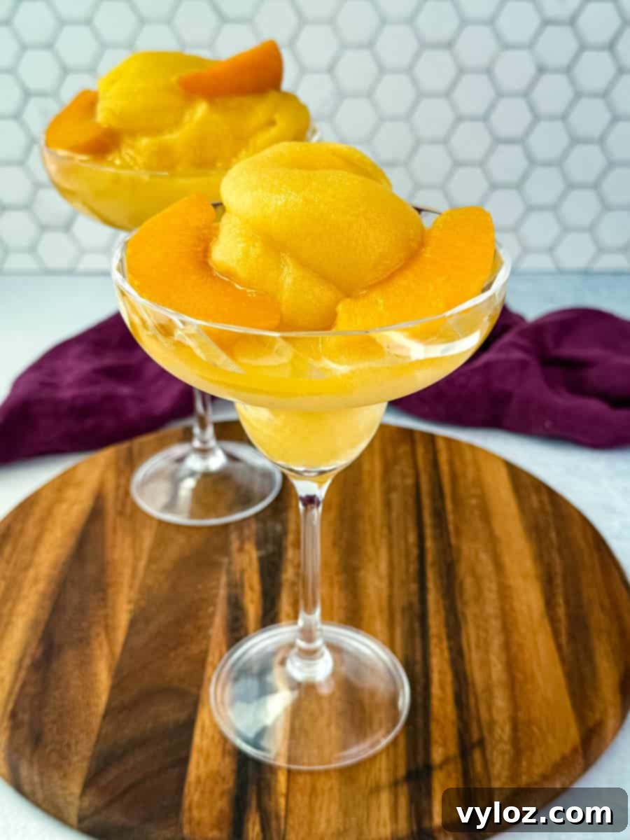 Two elegant cocktail glasses brimming with thick, frosty peach Bellini slush, beautifully garnished with fresh peach slices, set invitingly on a rustic wooden board.
