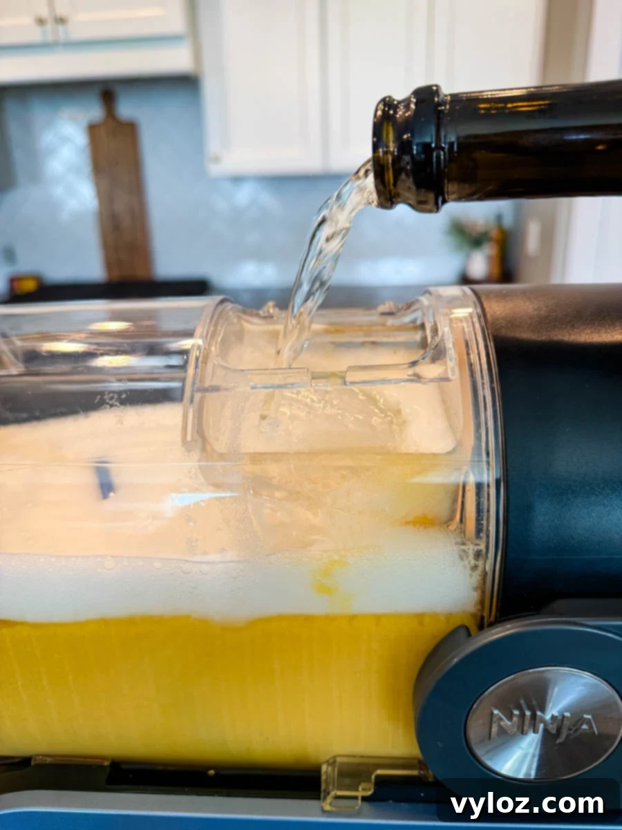 Effervescent Prosecco is gently poured into the Ninja Slushi container, mixing with the vibrant peach base, signaling the start of the freezing process for a delightful frozen Bellini.