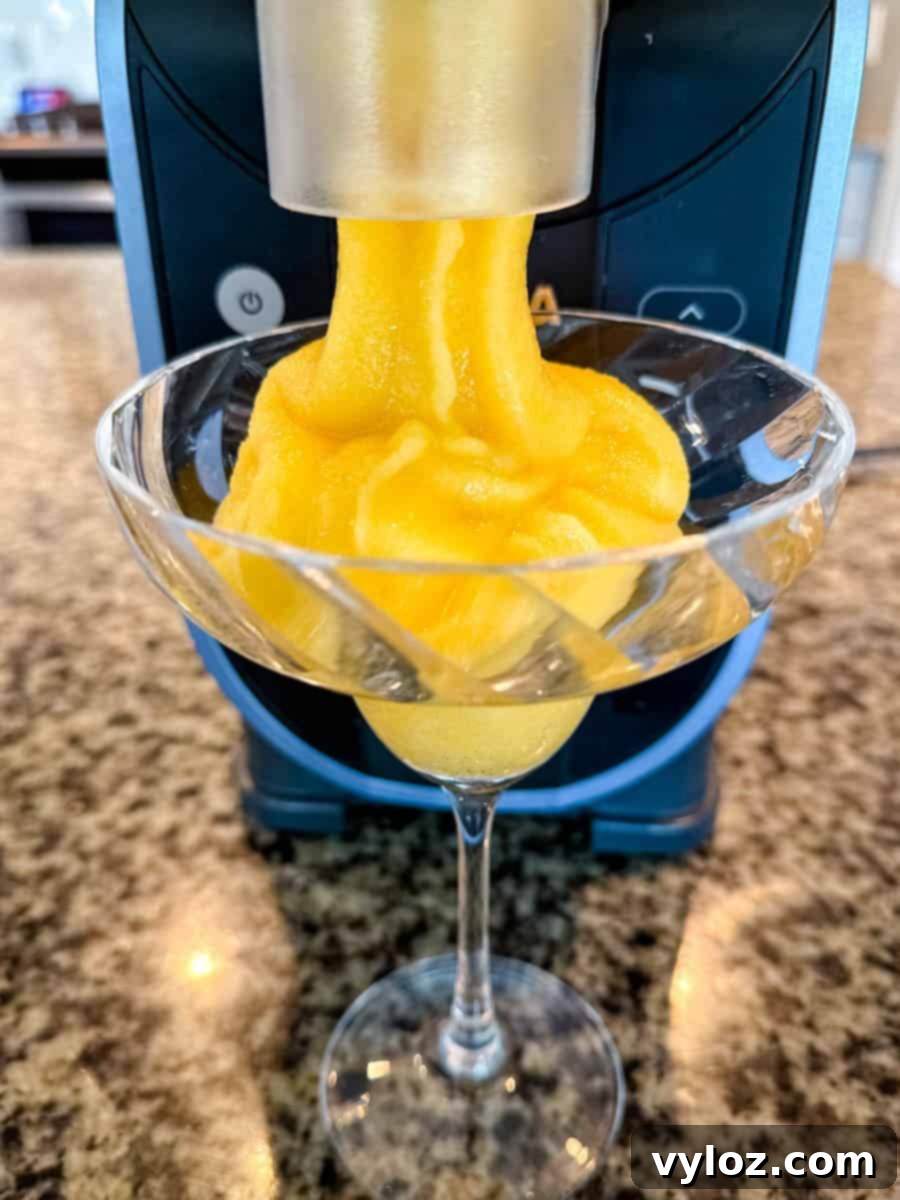 A stream of perfectly frozen peach Bellini slush cascades into a waiting cocktail glass from the Ninja Slushi machine's convenient spout, ready to be served and enjoyed.