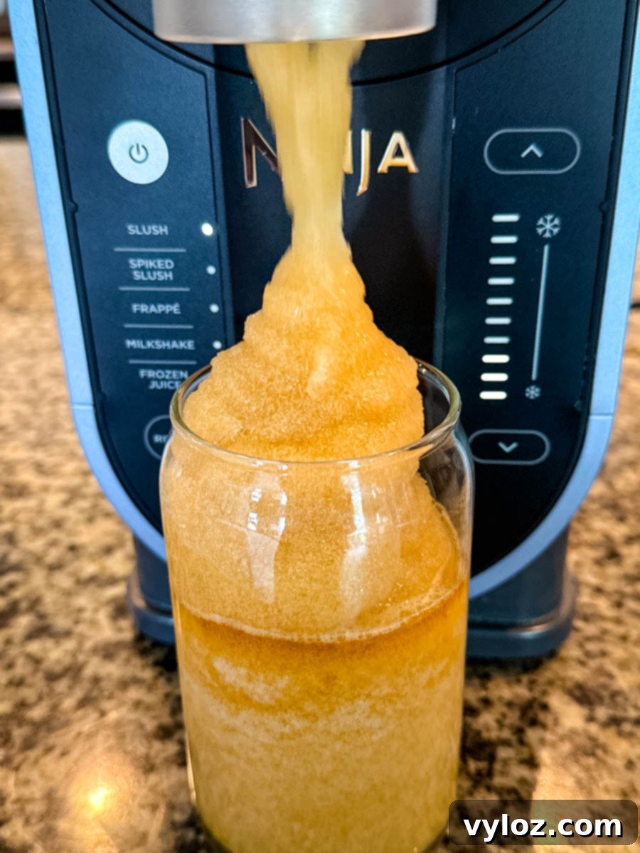 The Ninja Slushi machine efficiently dispensing a perfect mound of icy iced tea slush into a clear glass, demonstrating its smooth, ready-to-serve consistency.