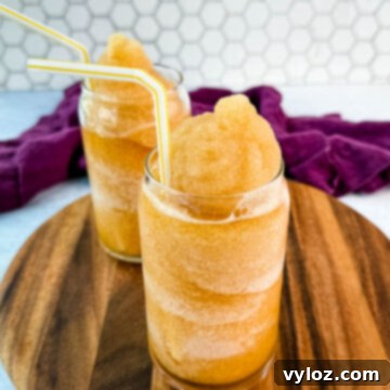 Closer side angle of iced tea slush in two glasses with yellow-striped straws on a wooden board, highlighting the refreshing texture.