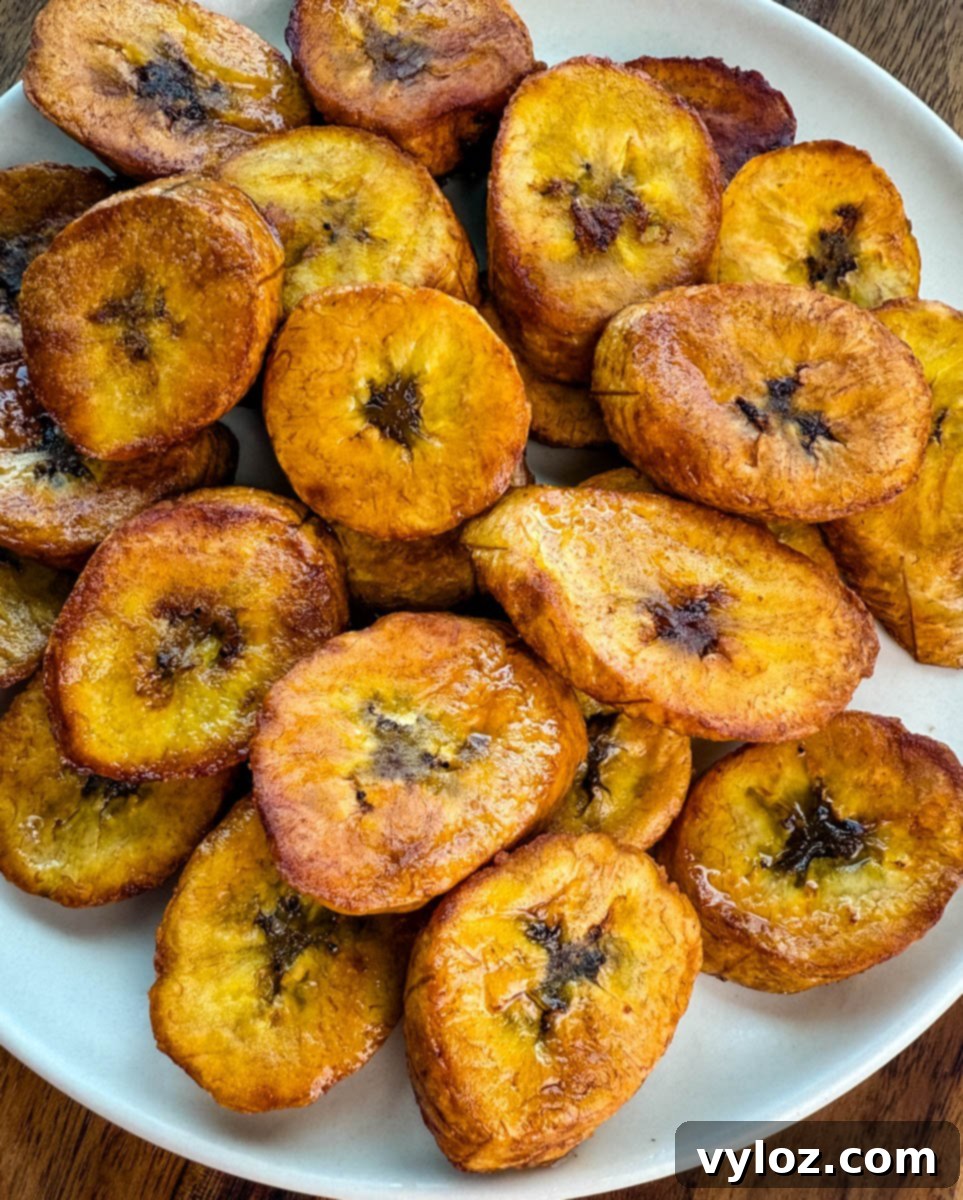 Close-up of perfectly golden-brown fried plantains stacked on a plate, glistening with oil.