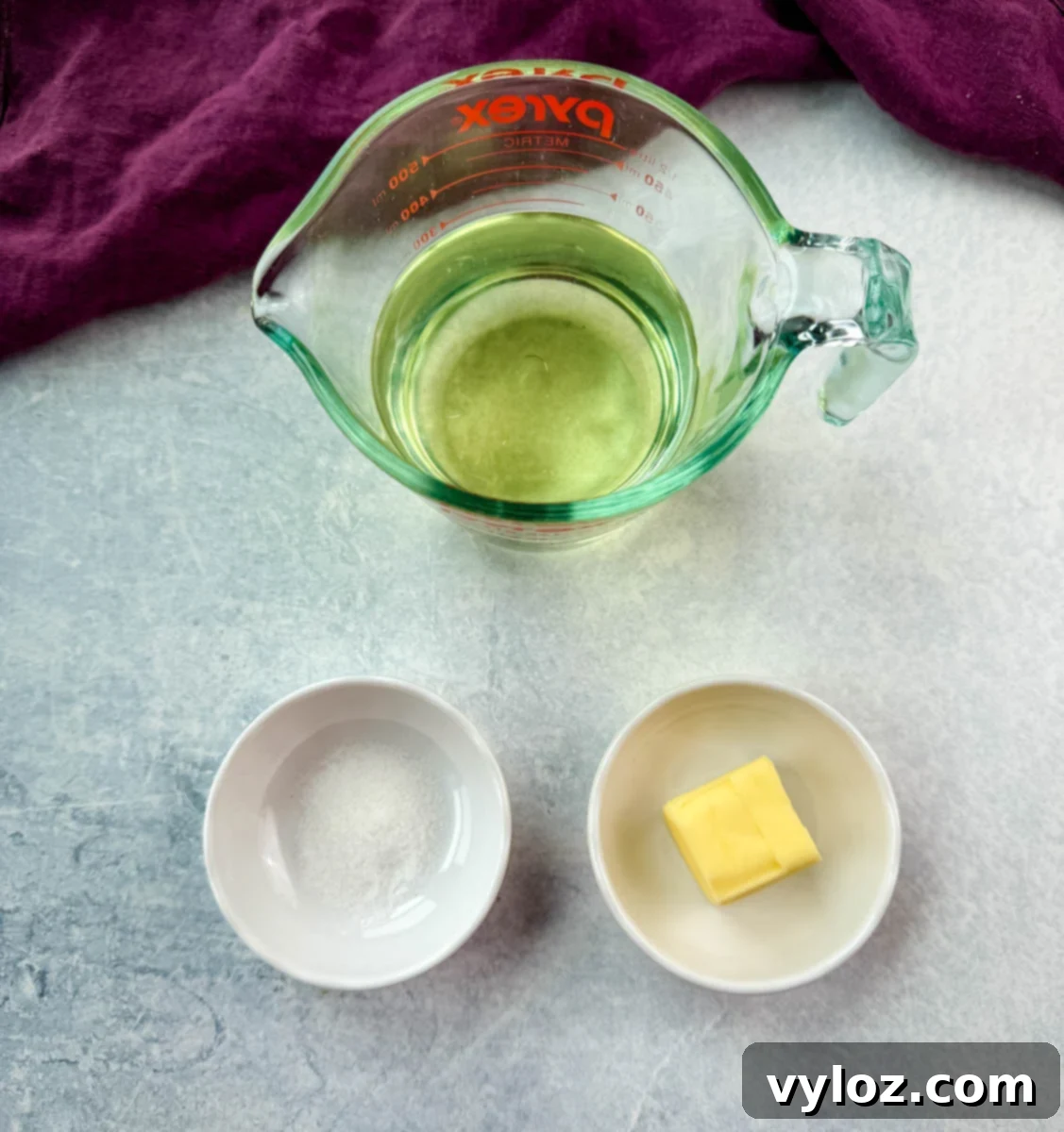 A measuring cup of oil with small bowls of butter and salt on a light background.