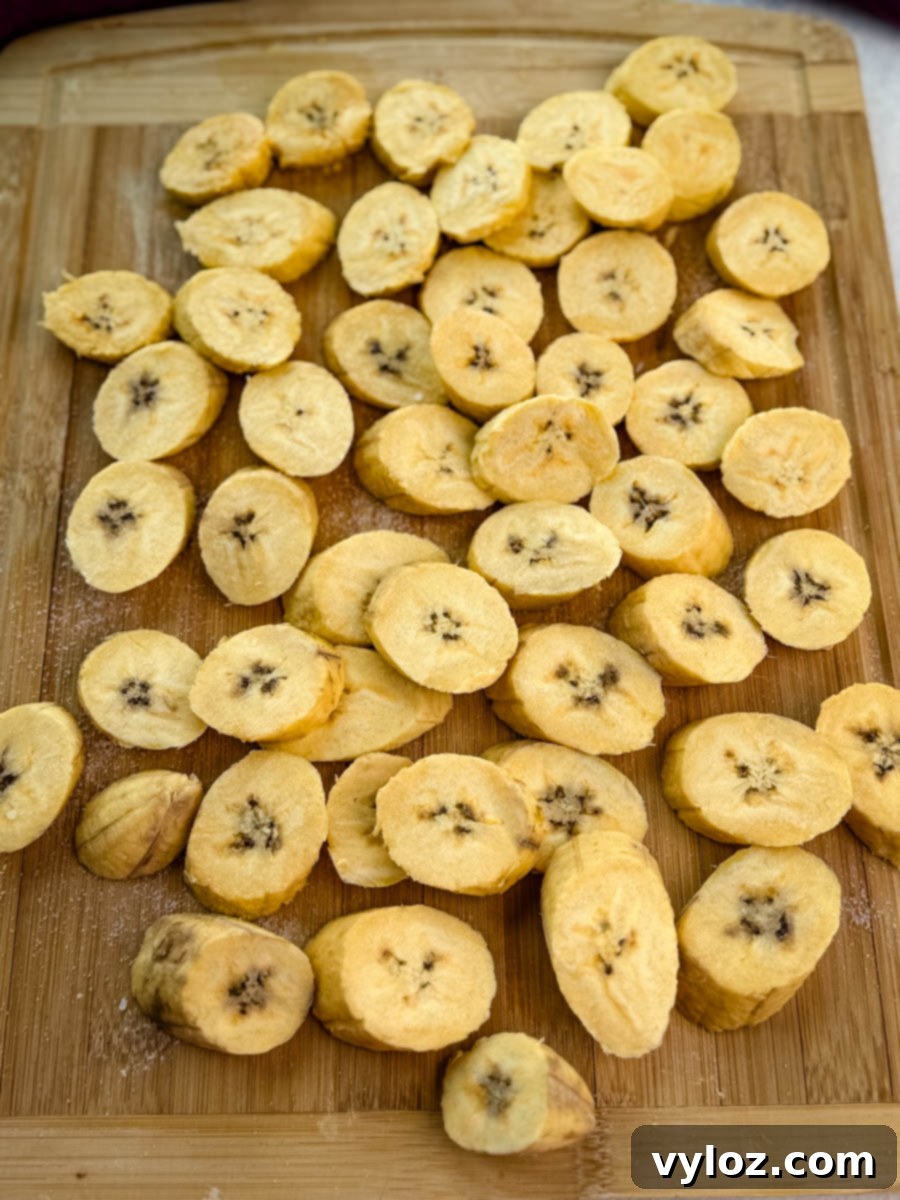 Raw, sliced plantains arranged in a single layer in an air fryer basket before cooking.