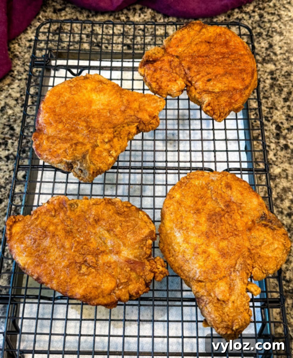 Crispy Southern Fried Pork Chops 11 Four freshly fried pork chops resting on a wire rack to cool and stay crispy, a vital step for perfect texture.