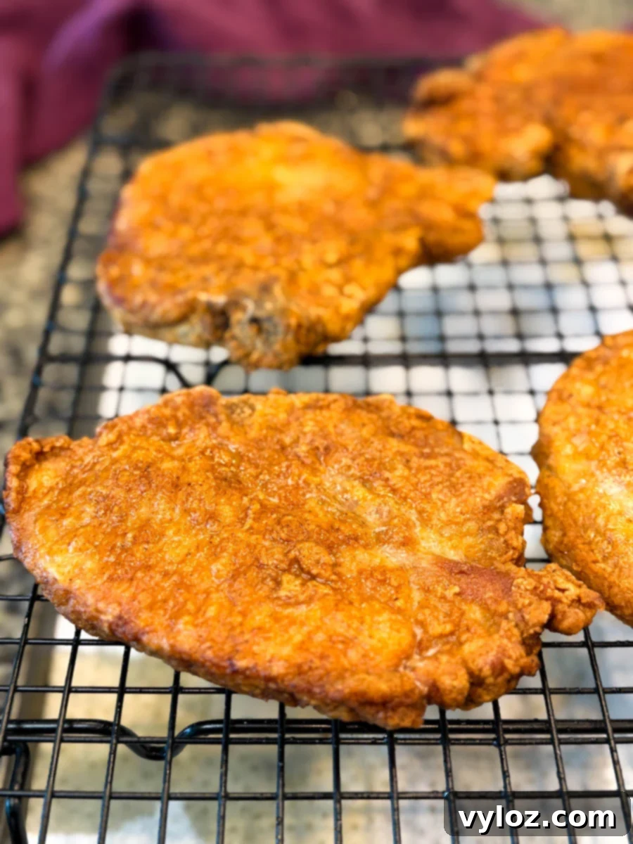 Crispy Southern Fried Pork Chops 12 Close-up shot of crispy golden pork chops on a wire rack after frying, showcasing their perfect texture.