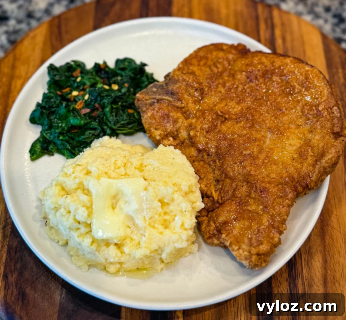 Crispy Southern Fried Pork Chops 4 A plate of fried pork chop served with buttery cheese grits and sautéed greens, illustrating a complete Southern meal.