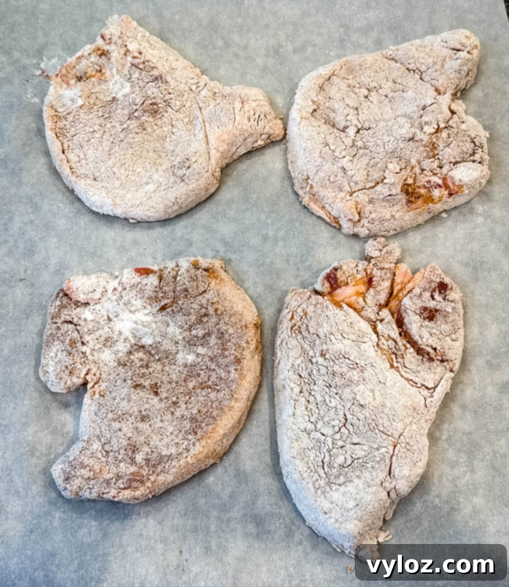 Crispy Southern Fried Pork Chops 9 Raw seasoned pork chops coated in flour, ready for frying.