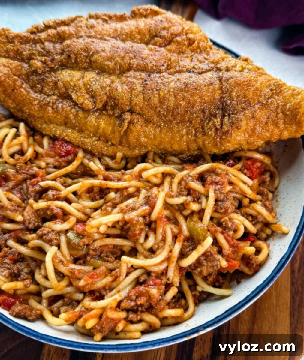 Close-up shot of a crispy golden-brown fried catfish fillet elegantly resting on top of a generous portion of rich, chunky meat spaghetti sauce, highlighting the texture contrast.
