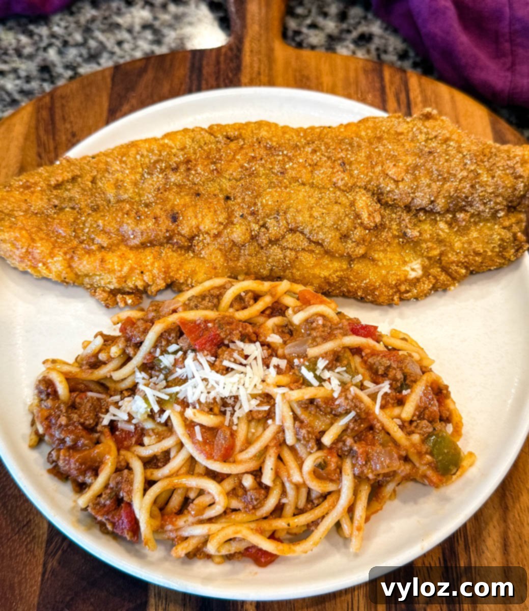 A perfectly plated serving with one large, golden-brown fried catfish fillet resting beside a generous scoop of spaghetti, lavishly topped with shredded Parmesan cheese.