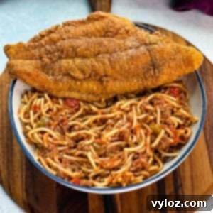 Fried catfish served with spaghetti on a white plate, garnished with shredded cheese, all placed on a wooden board.