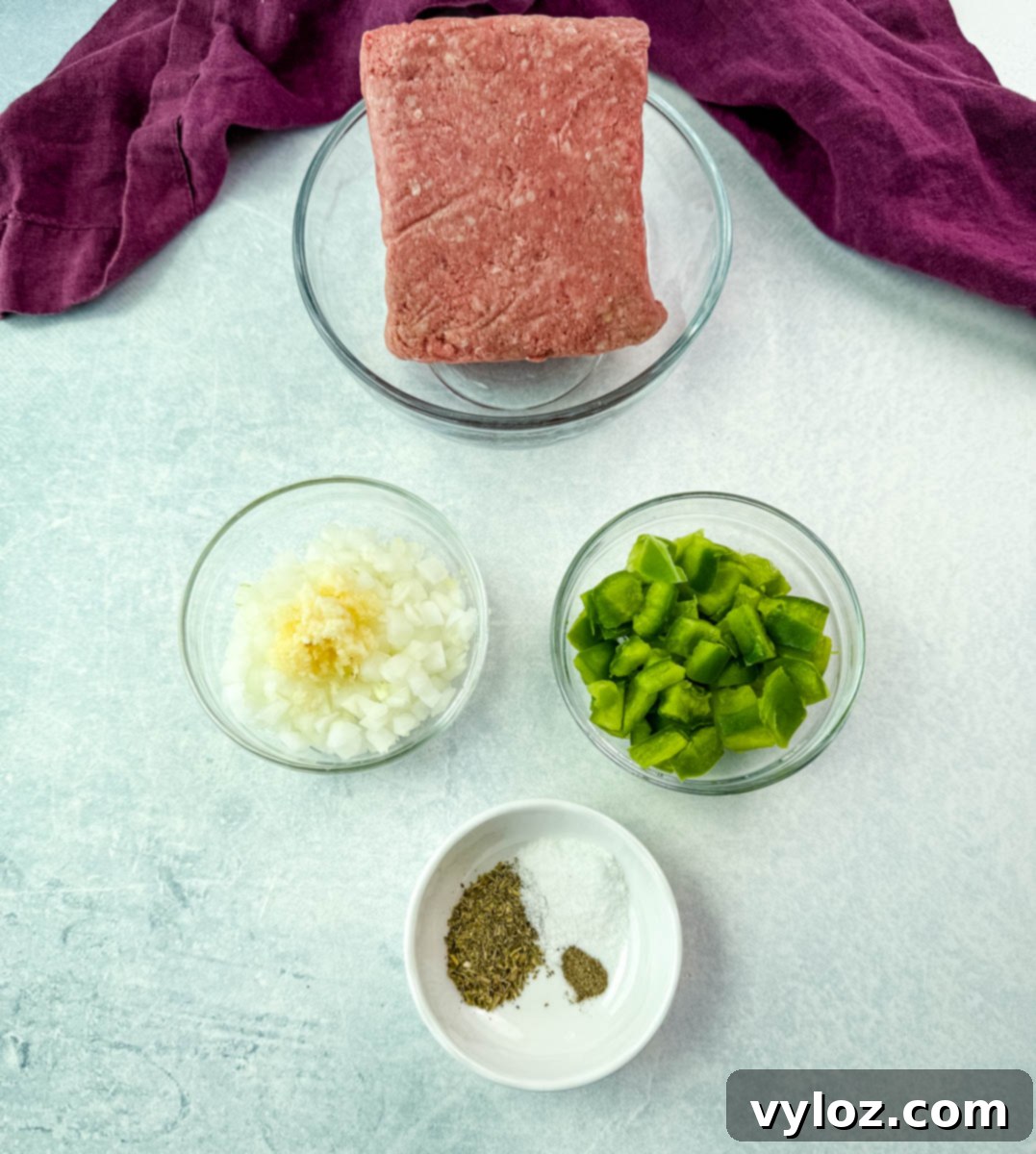 Overhead view of prepared ingredients for spaghetti, featuring raw ground meat in a mixing bowl, finely chopped onions with minced garlic, diced green bell peppers, and a small bowl of dry seasonings, all neatly displayed on a light blue kitchen surface.