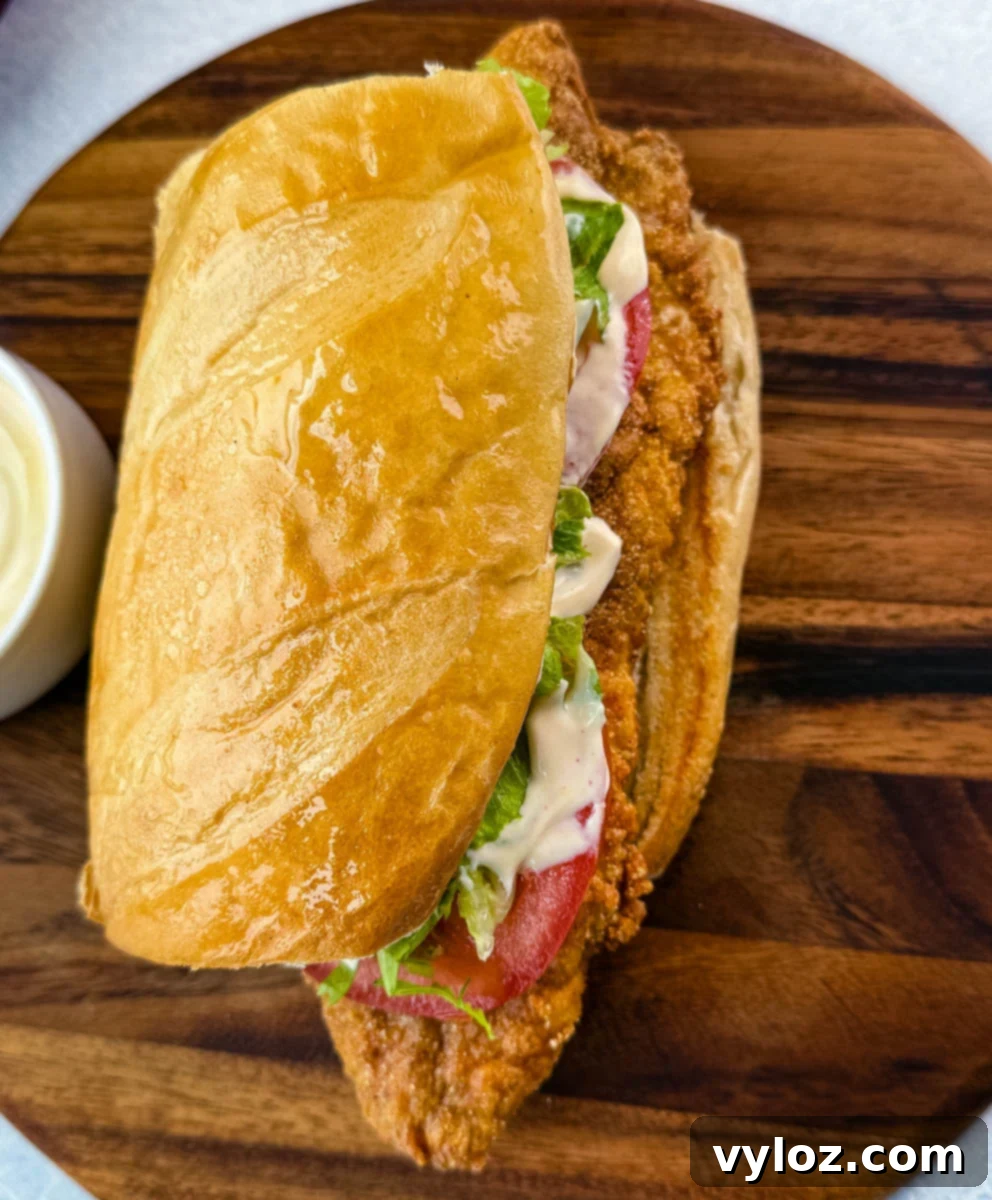 Overhead shot of the sandwich with a shiny top bun and toppings visible. A bowl of dipping sauce is placed beside it on a wooden board.