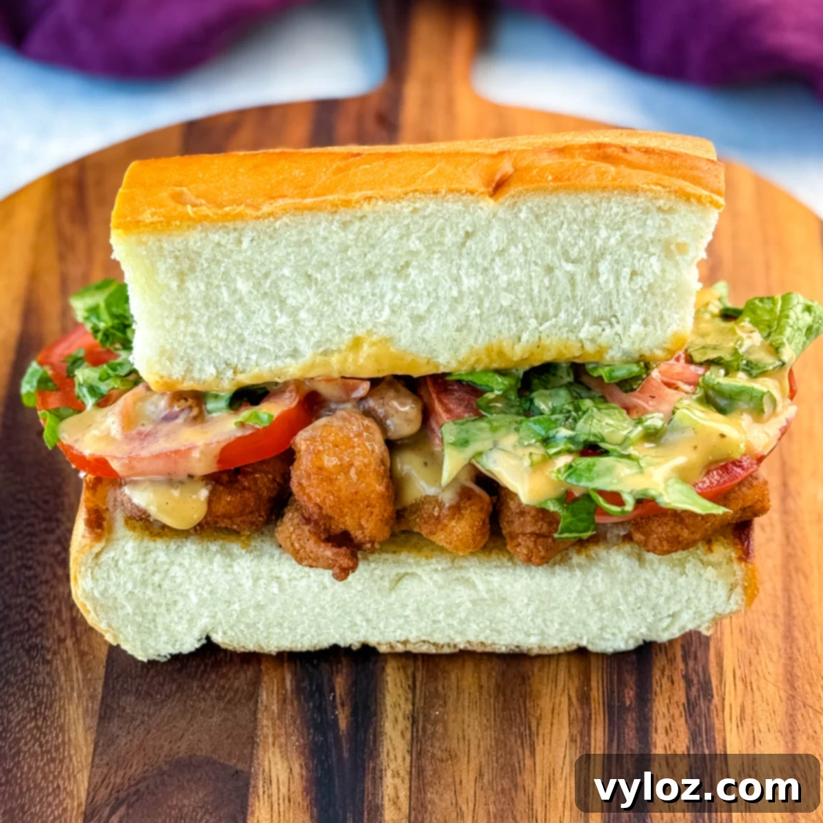 Crispy Chicken Po Boy 2 Centered image of a crispy chicken po' boy sandwich on a cutting board, showcasing layers of fried chicken, tomato, lettuce, and sauce, surrounded by chips. A vibrant and appealing meal.