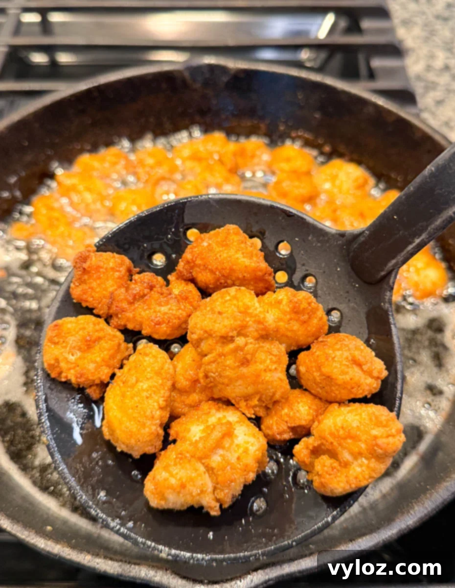 Crispy Chicken Po Boy 7 A slotted spoon lifting crispy golden-brown fried chicken bites out of hot oil in a cast iron skillet, with oil bubbling around. Captures the moment of perfect frying.