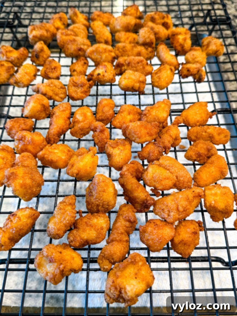 Crispy Chicken Po Boy 8 Golden brown fried chicken bites cooling on a wire rack over paper towels, allowing excess oil to drip away while maintaining crispiness. Demonstrates proper draining technique.