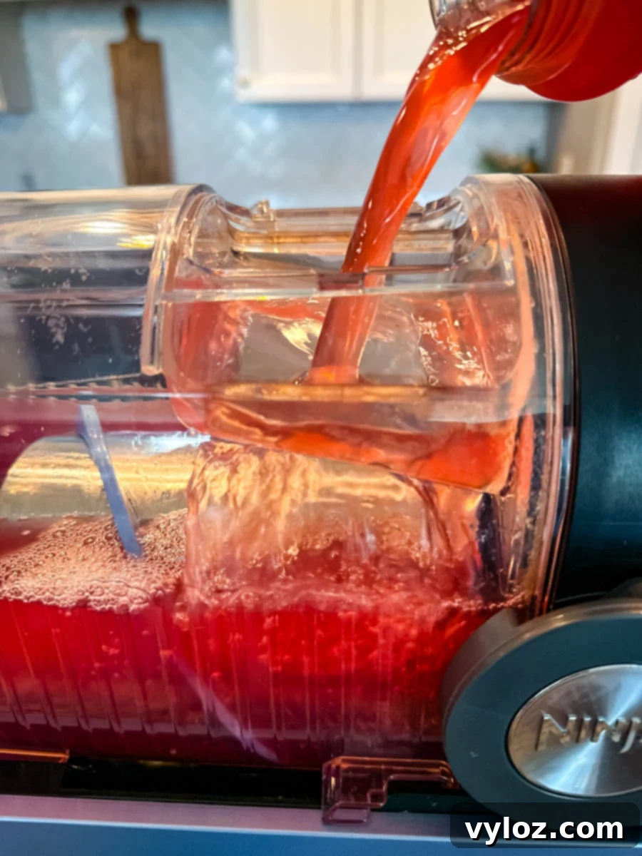 Close-up of fruit punch being poured into the Ninja Slushi machine, showing the red liquid flowing into the clear container filled with ice.