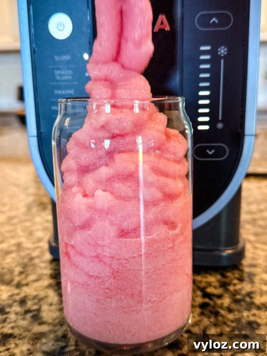 The pink fruit punch slush being dispensed from the Ninja Slushi machine into a clear glass, creating tall, swirled layers.