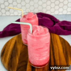 Two glasses of pink fruit punch slush placed side-by-side on a wooden tray in front of a white hexagon tile wall, each with a colorful striped straw.