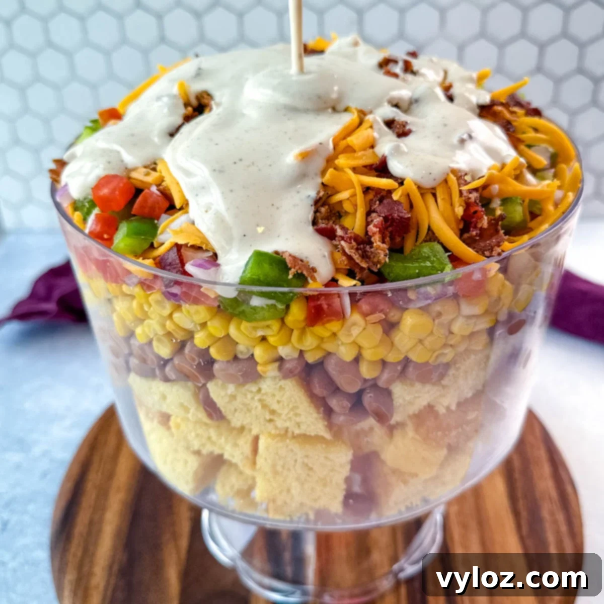 Creamy ranch dressing being generously poured over the artfully layered Southern Cornbread Salad in a clear glass trifle dish, highlighting its rich textures and vibrant colors.