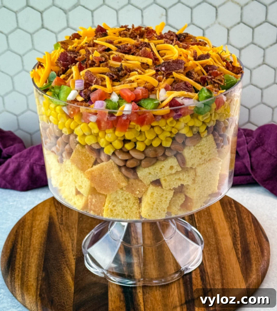 A complete, beautifully layered Southern Cornbread Salad presented in a clear glass trifle bowl, expertly placed on a rustic wooden serving board, ready to be enjoyed.