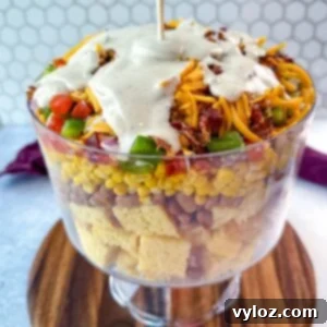 Ranch dressing being poured over the top of the layered Southern Cornbread Salad in a glass trifle dish.
