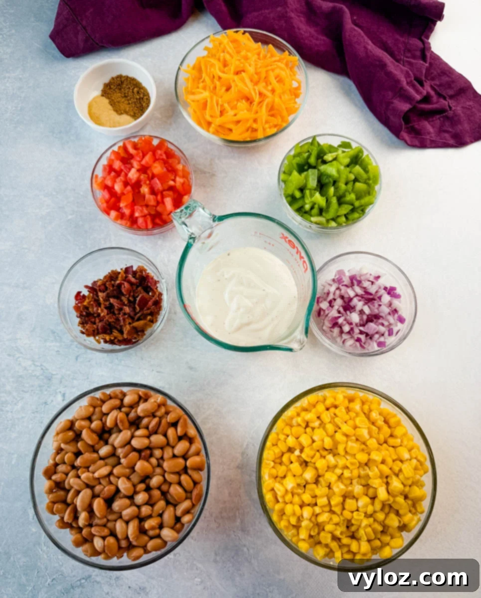 An overhead shot showcasing all the fresh and flavorful ingredients for Southern Cornbread Salad, including vibrant pinto beans, golden corn, crispy bacon, shredded cheddar cheese, diced tomatoes, green bell peppers, red onion, creamy ranch dressing, and a custom seasoning blend with Creole seasoning and garlic powder, all arranged in separate bowls.